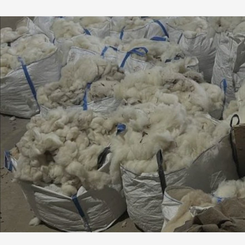 Bales of white wool in large bags with blue straps on a concrete floor.